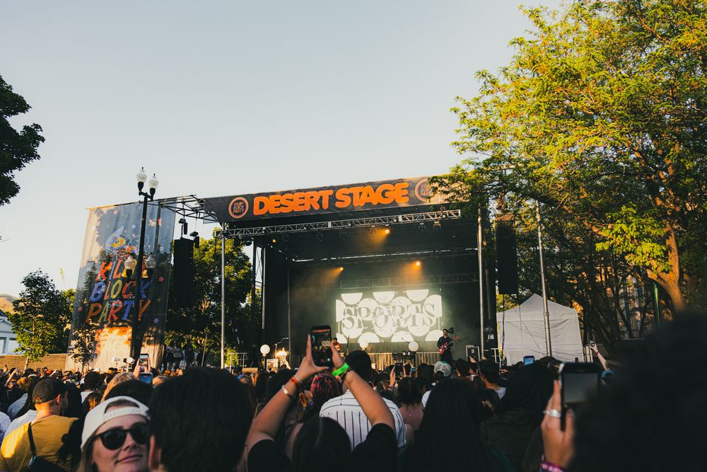 Crowd at Desert Stage outdoor music festival with large LED screen and trees in background.