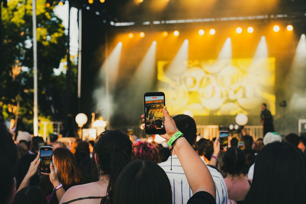 Crowd at outdoor music festival filming lit stage with smartphones at night.