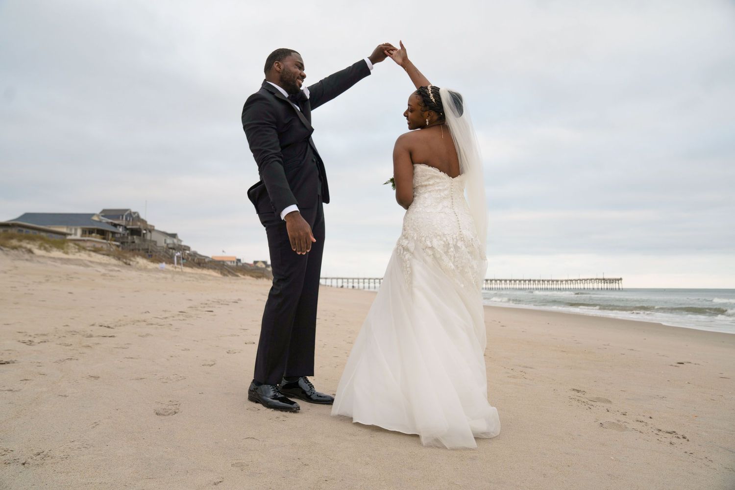A couple performs a unity ceremony on a cloudy beach with sand dunes in the background.