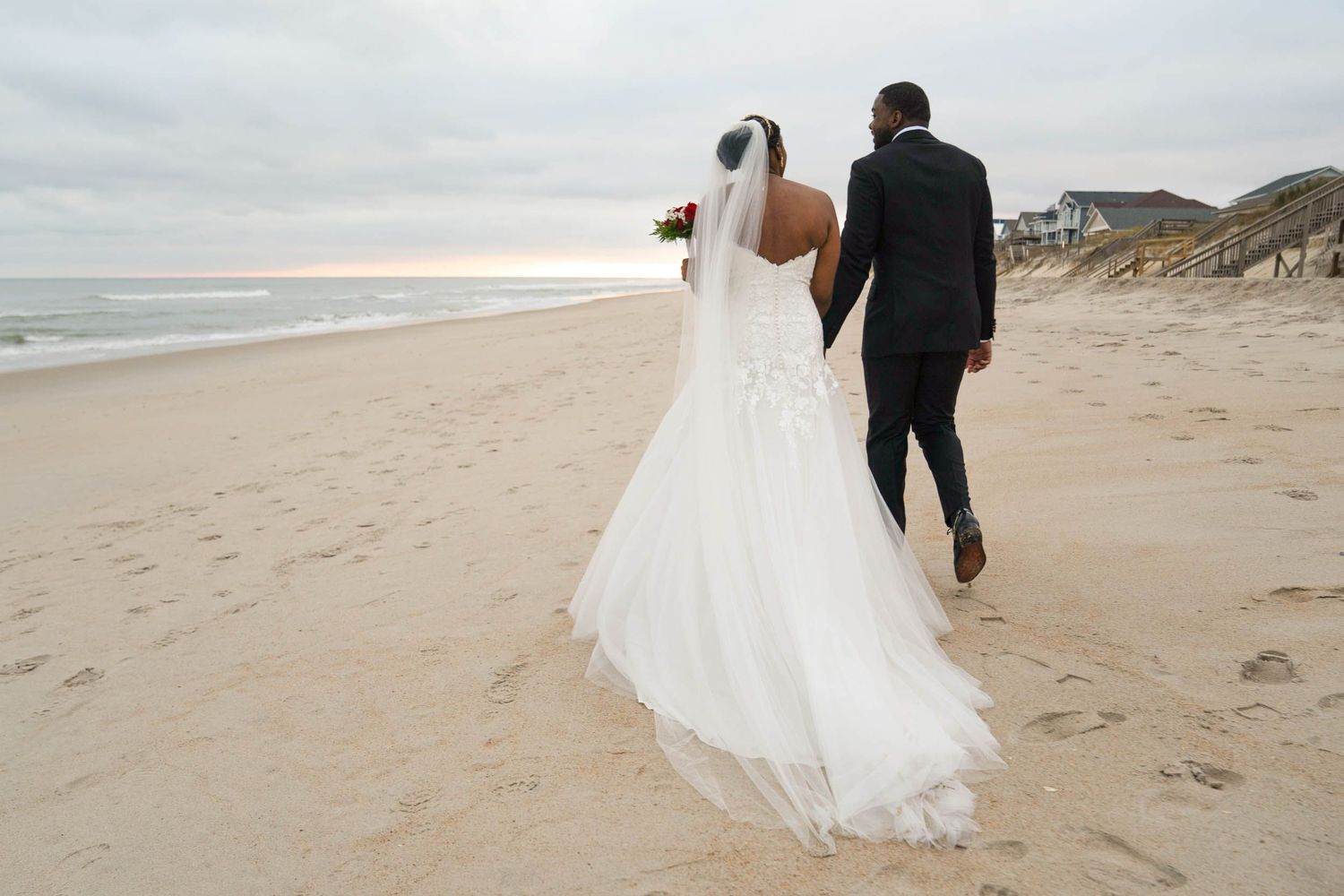 A couple walks along a scenic beach with waves and cliffs in the background.
