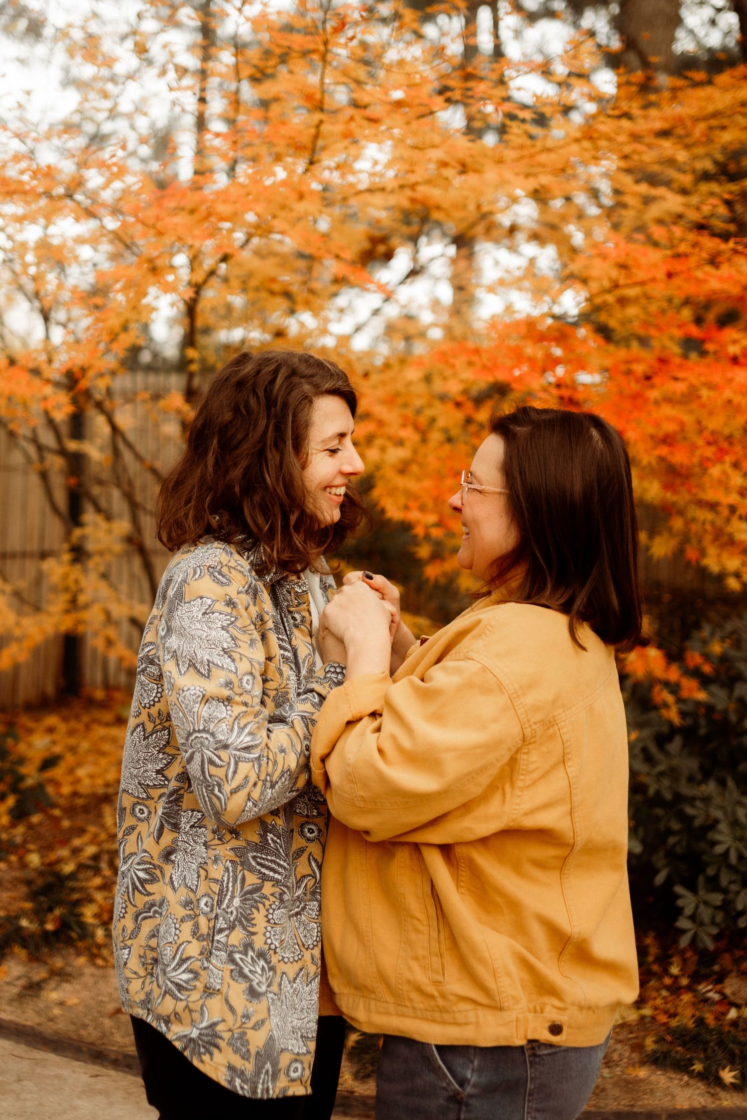 Two people share a joyful moment together surrounded by vibrant orange autumn foliage in a park setting.