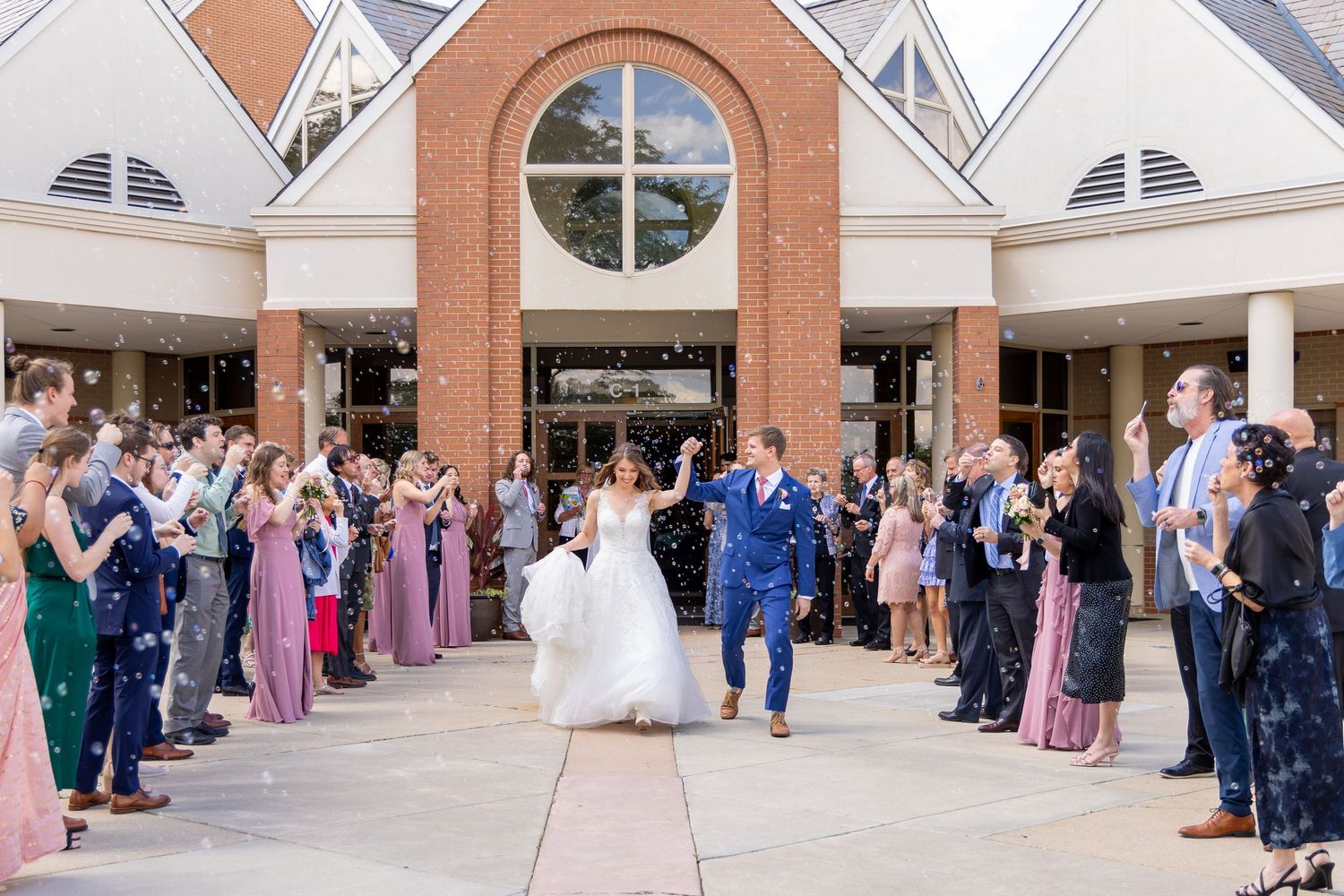 Wedding guests gather in formal attire at an elegant venue with brick columns and arched windows. Dayton Ohio church wedding.