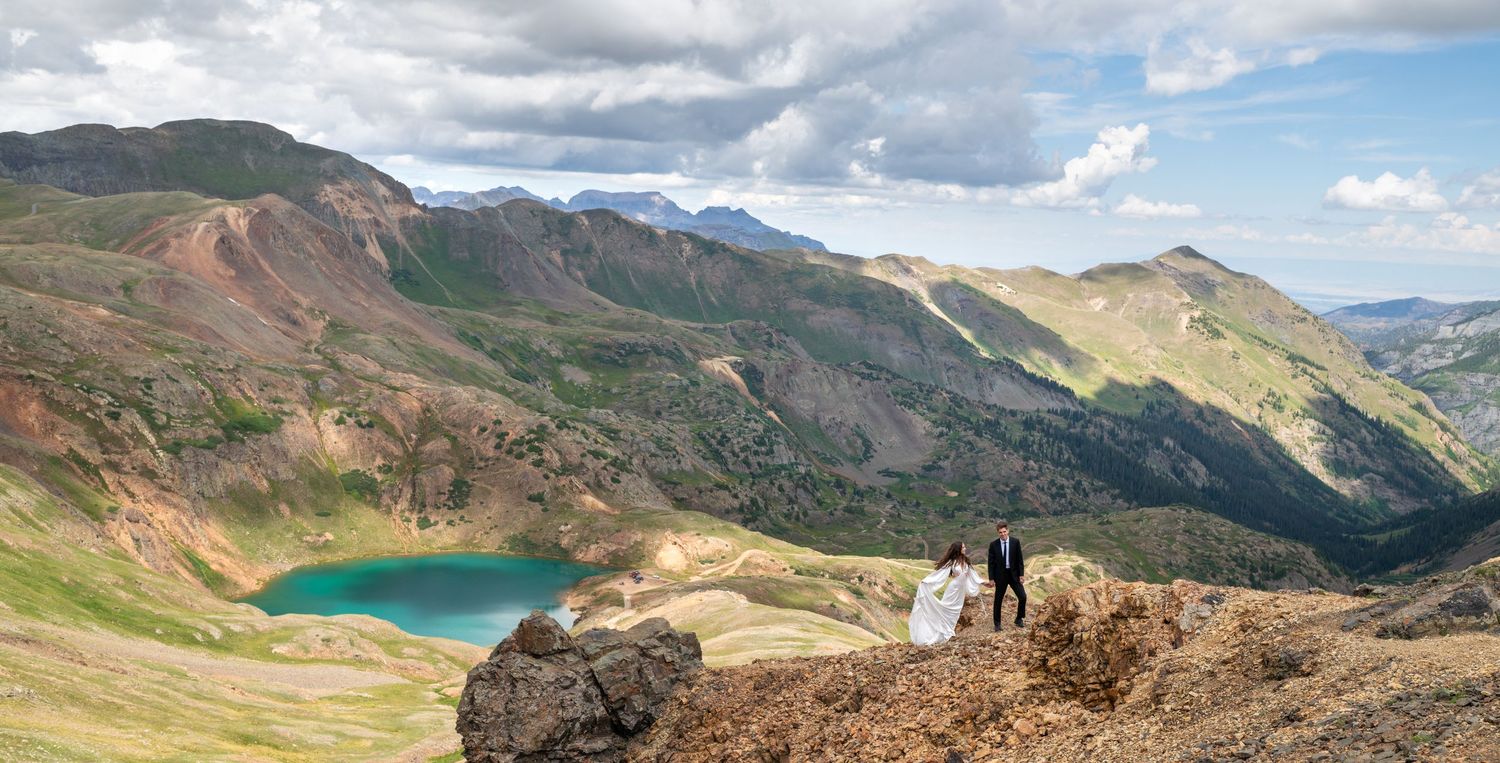 Bride and groom walking hand in hand through a golden meadow with autumn aspen trees and Rocky Mountains backdrop.