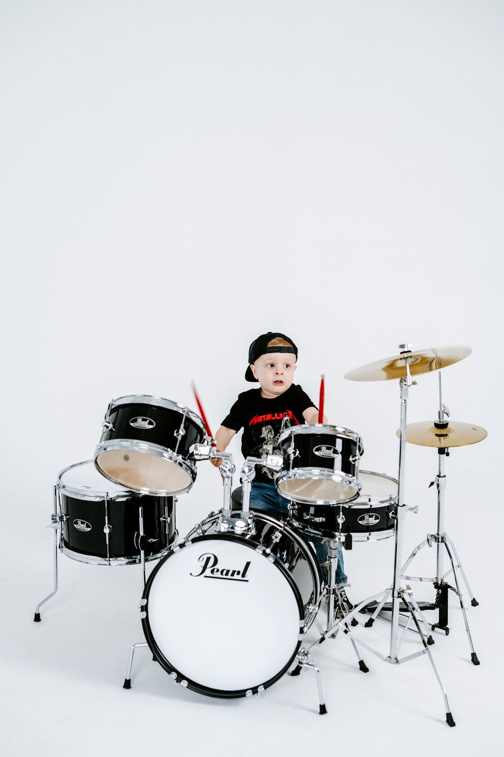 Young drummer plays a black Pearl drum kit against a white background.