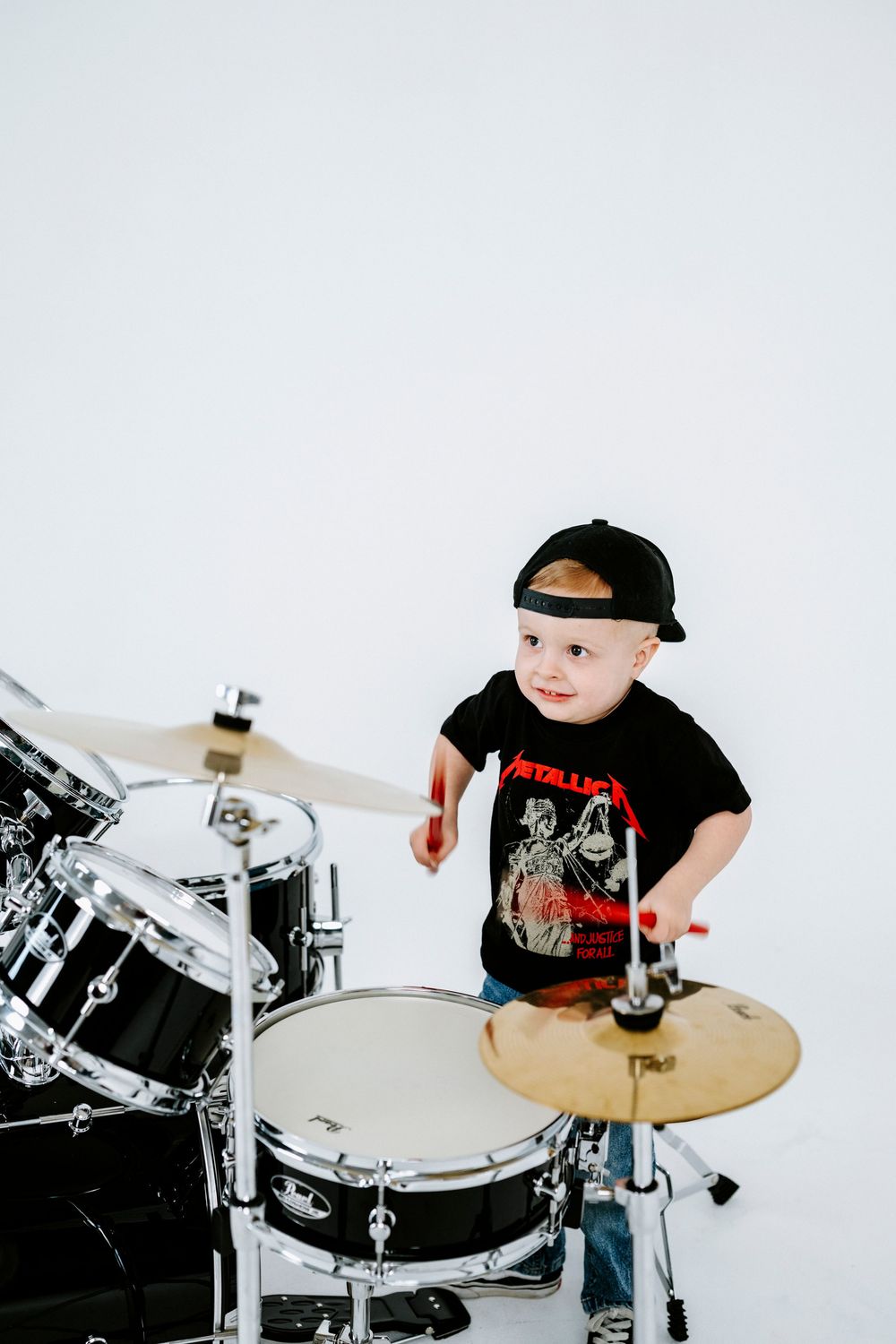 A young drummer wearing a Metallica t-shirt plays on a drum set against a white background.