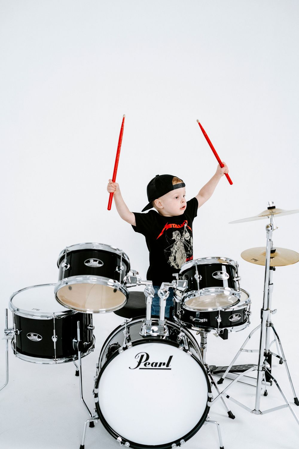 A sequence of four images showing a drummer in action playing a black Pearl drum kit against a white background.
