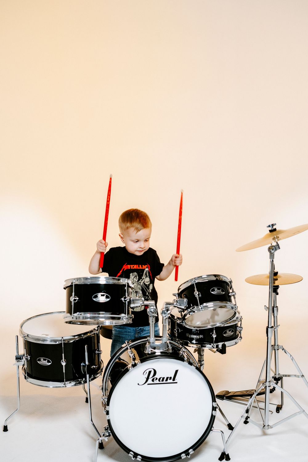 Small child playing on a black Pearl drum set against a white background.
