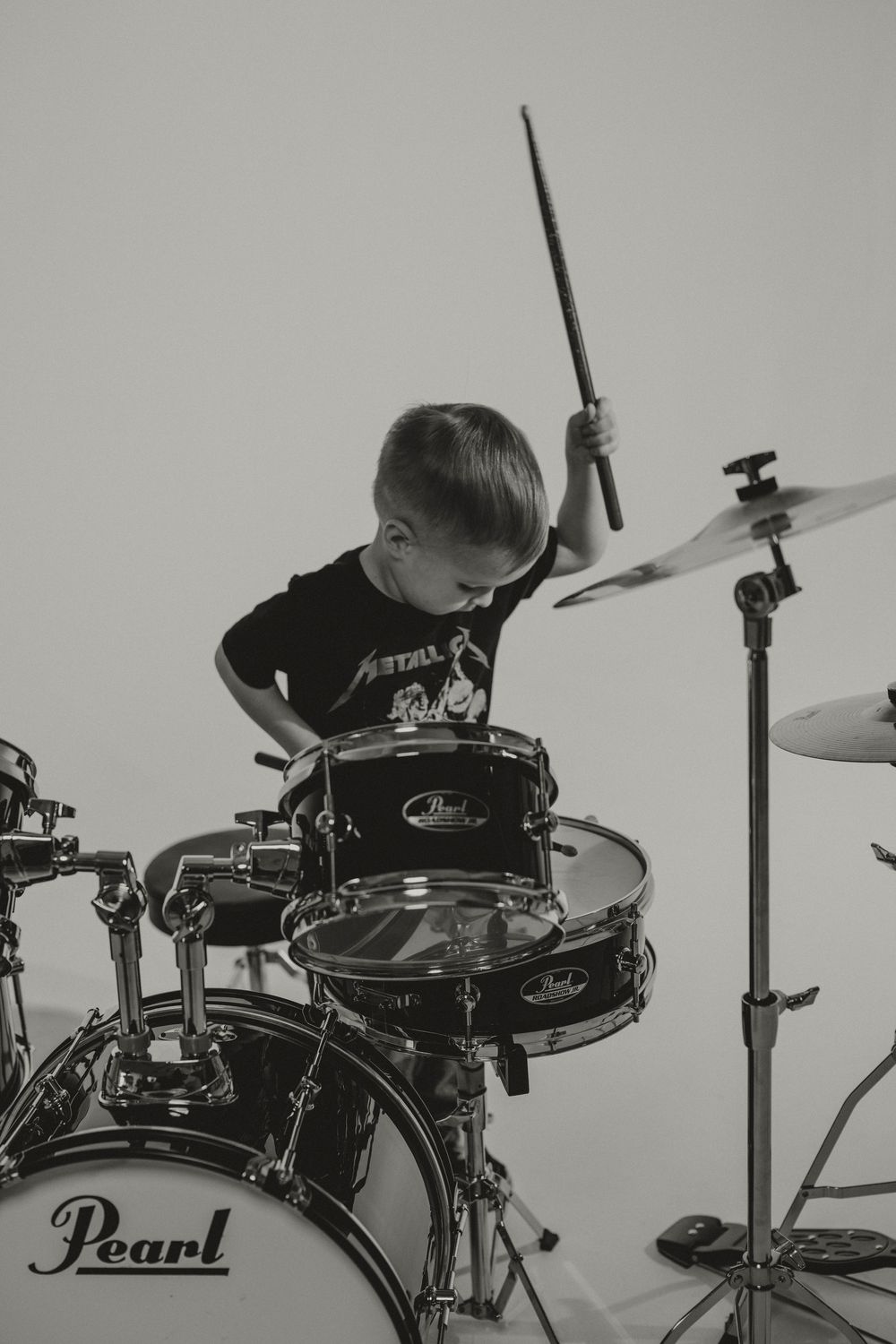 Young drummer plays on a Pearl drum set in black and white photograph.
