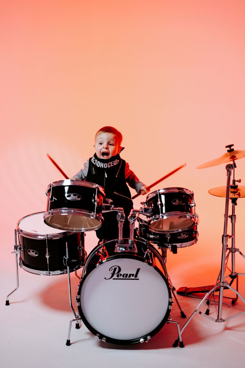 A series of photos showing a small drummer playing on a black Pearl drum kit against a pink background.