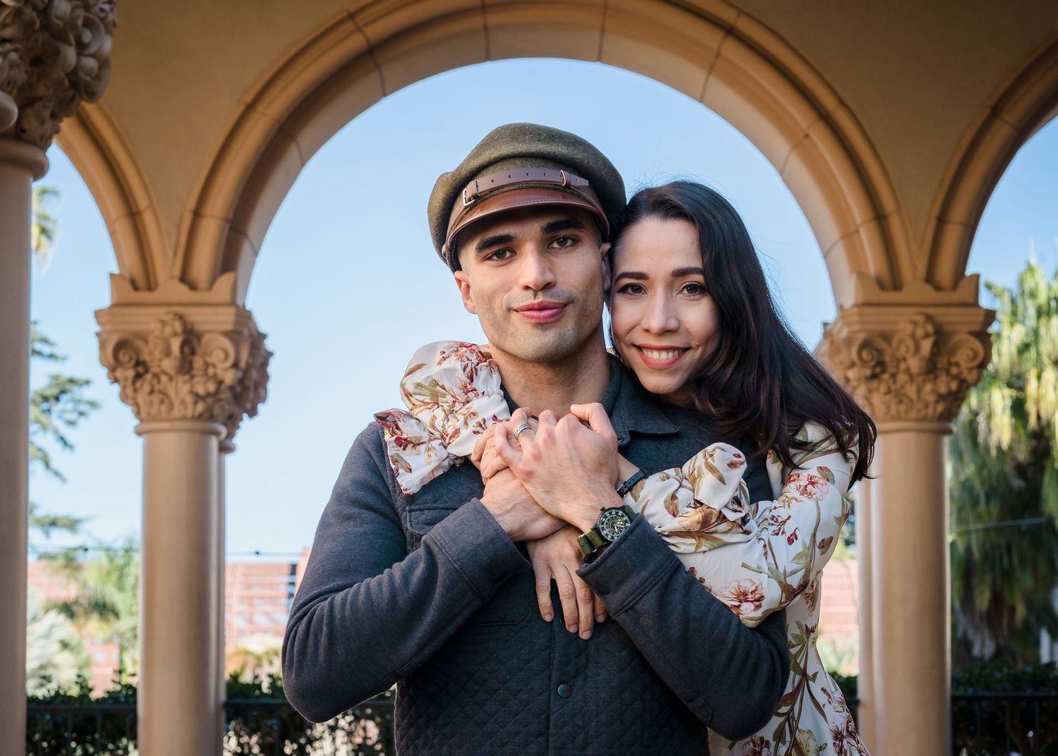 A couple poses together under ornate stone arches in a Mediterranean-style courtyard during a photoshoot.