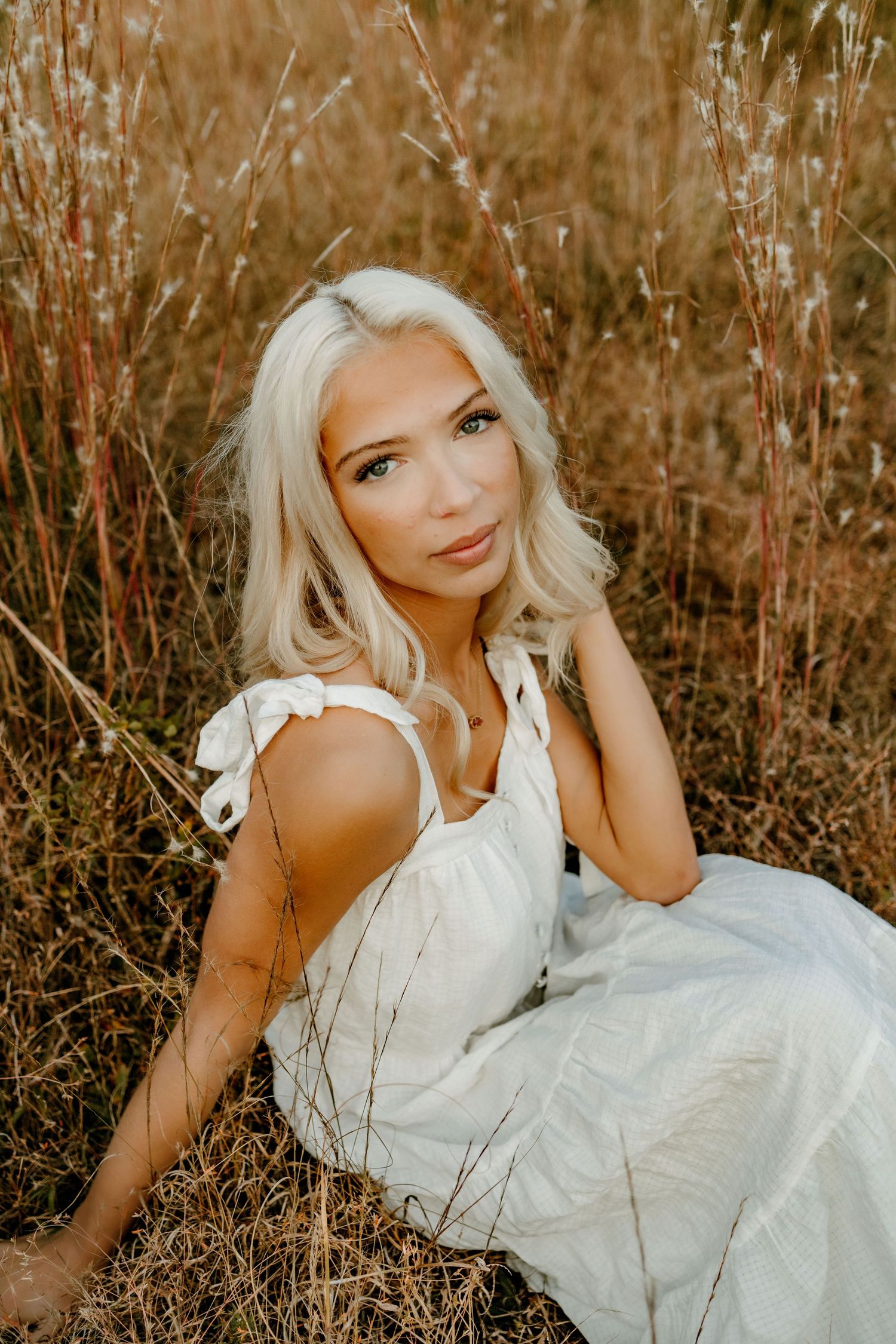 Woman in white dress poses gracefully in golden autumn field during sunset photoshoot.