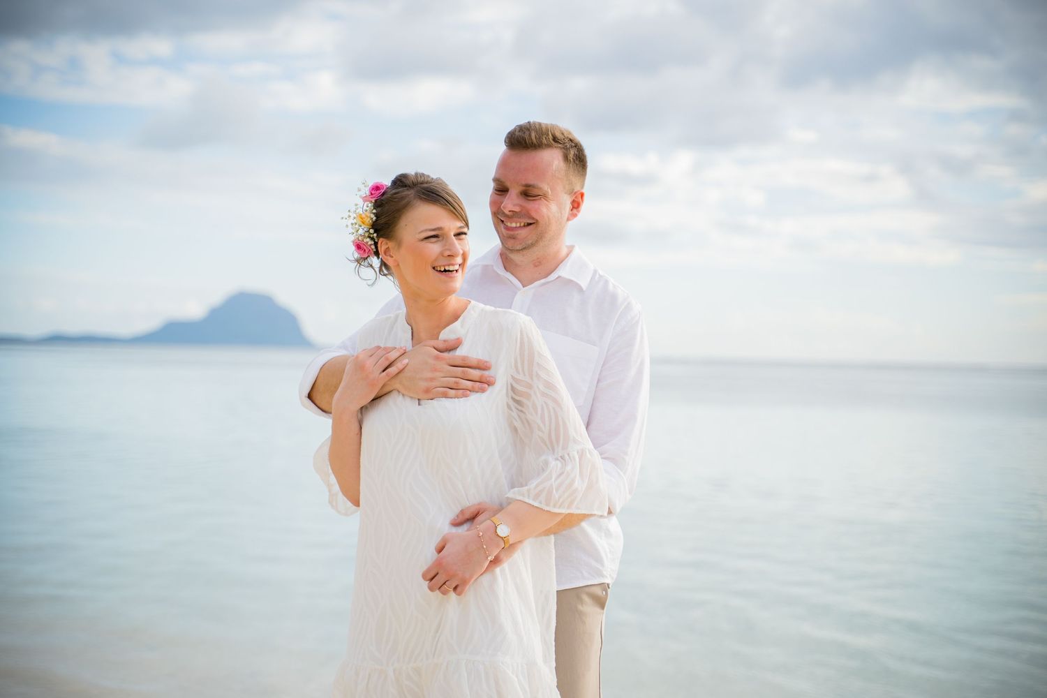 A couple in white clothing shares intimate moments during a romantic beach photoshoot with ocean views. Shot by Luminair Studio