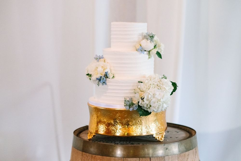 Three-tiered white and gold wedding cake decorated with fresh flowers on metallic cake stand.