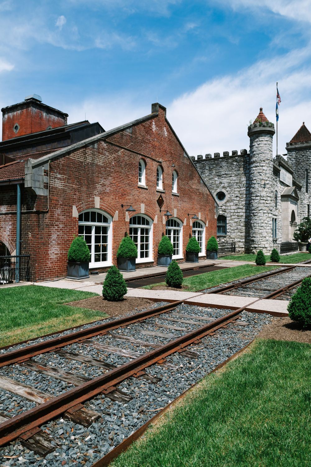 Historic brick and stone building exterior with train tracks leading to entrance along grassy landscaping.