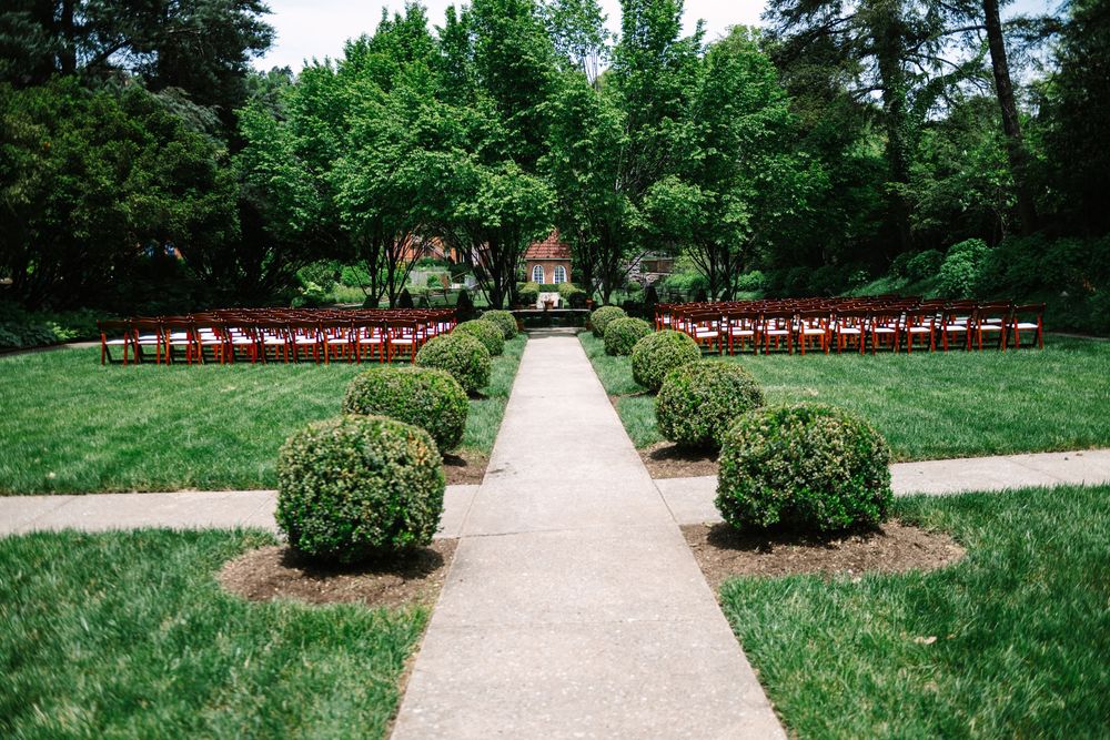 A winding stone path leads through a lush garden with rows of red chairs and ornamental shrubs on either side.