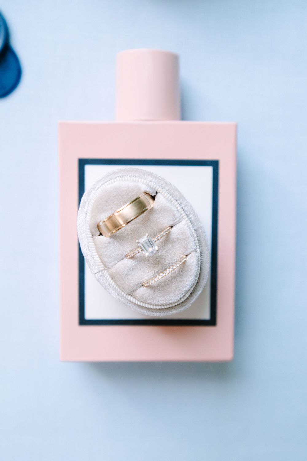 Wedding rings displayed on delicate white cushion with pink and blue background.