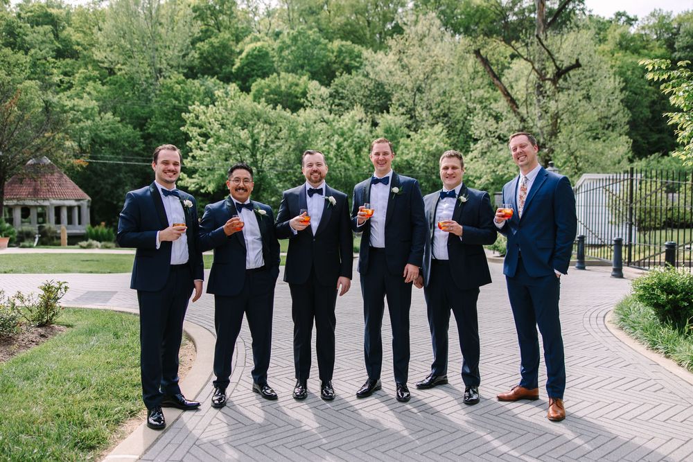 Wedding party wearing navy suits shows off their colorful socks while standing in a garden setting.