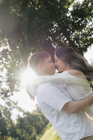 Couple sharing a romantic moment outdoors, bathed in golden sunlight beneath a lush green tree.