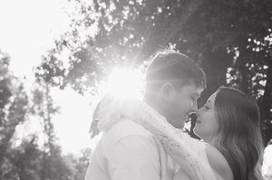 Black and white photo of a couple sharing a romantic moment outdoors with sunlight glowing behind them.