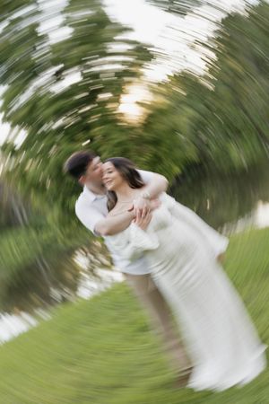 A groom lifts his bride in a romantic spinning embrace outdoors, captured with a dreamy radial blur effect.