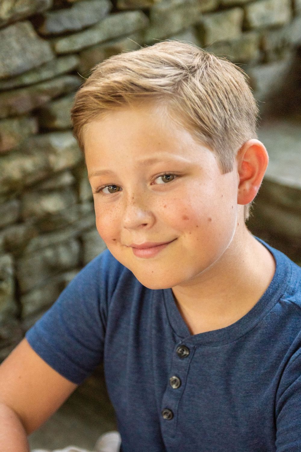 A series of four close-up photos showing a child in a navy blue shirt against a stone wall background.