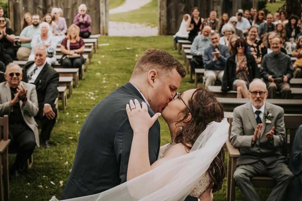 A couple shares a romantic kiss during their outdoor garden wedding ceremony while guests look on and smile.