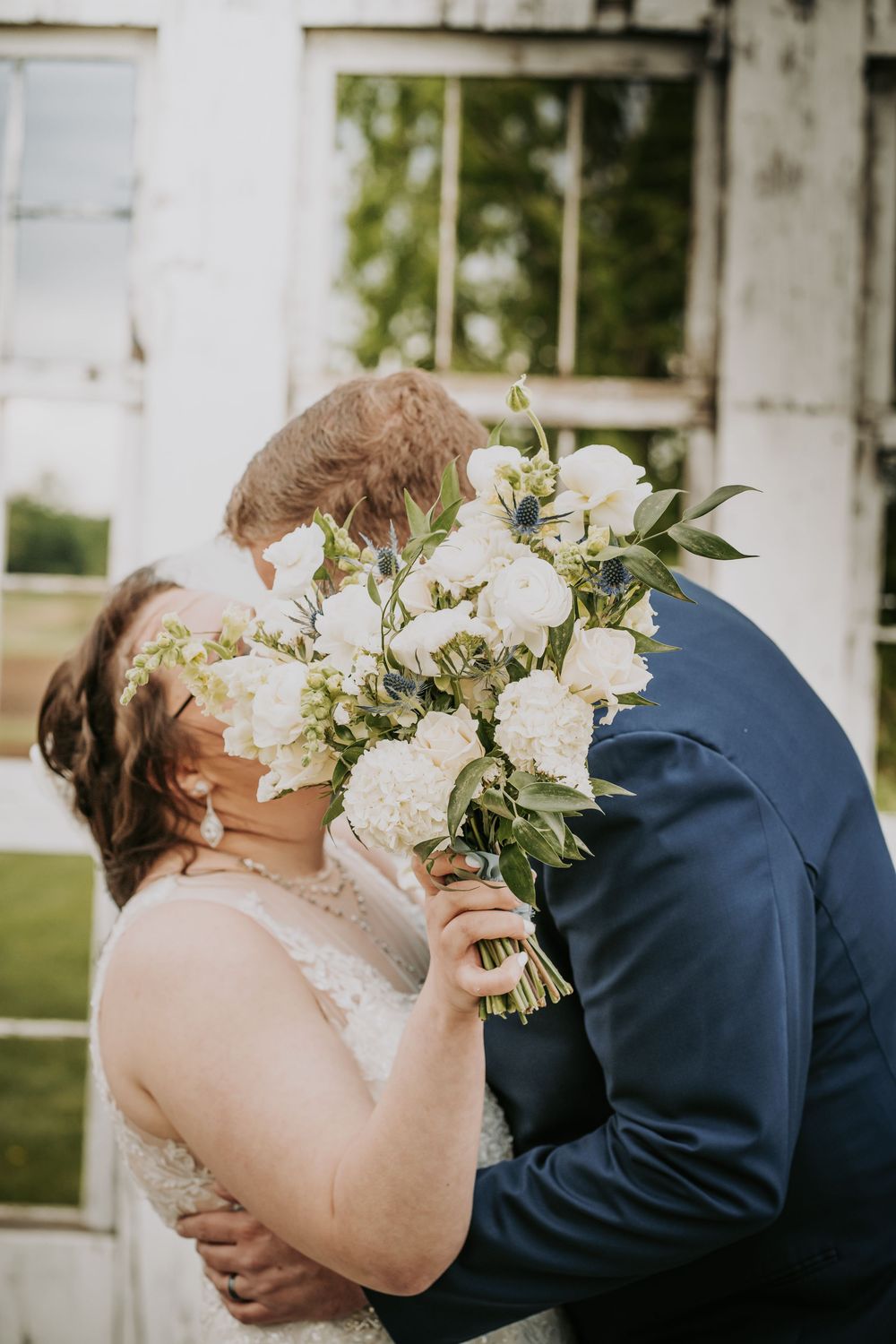 A couple shares a romantic moment behind a white bouquet during their outdoor wedding ceremony.