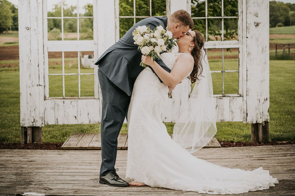 A romantic wedding couple shares a kiss in front of a rustic white barn door with window panes.