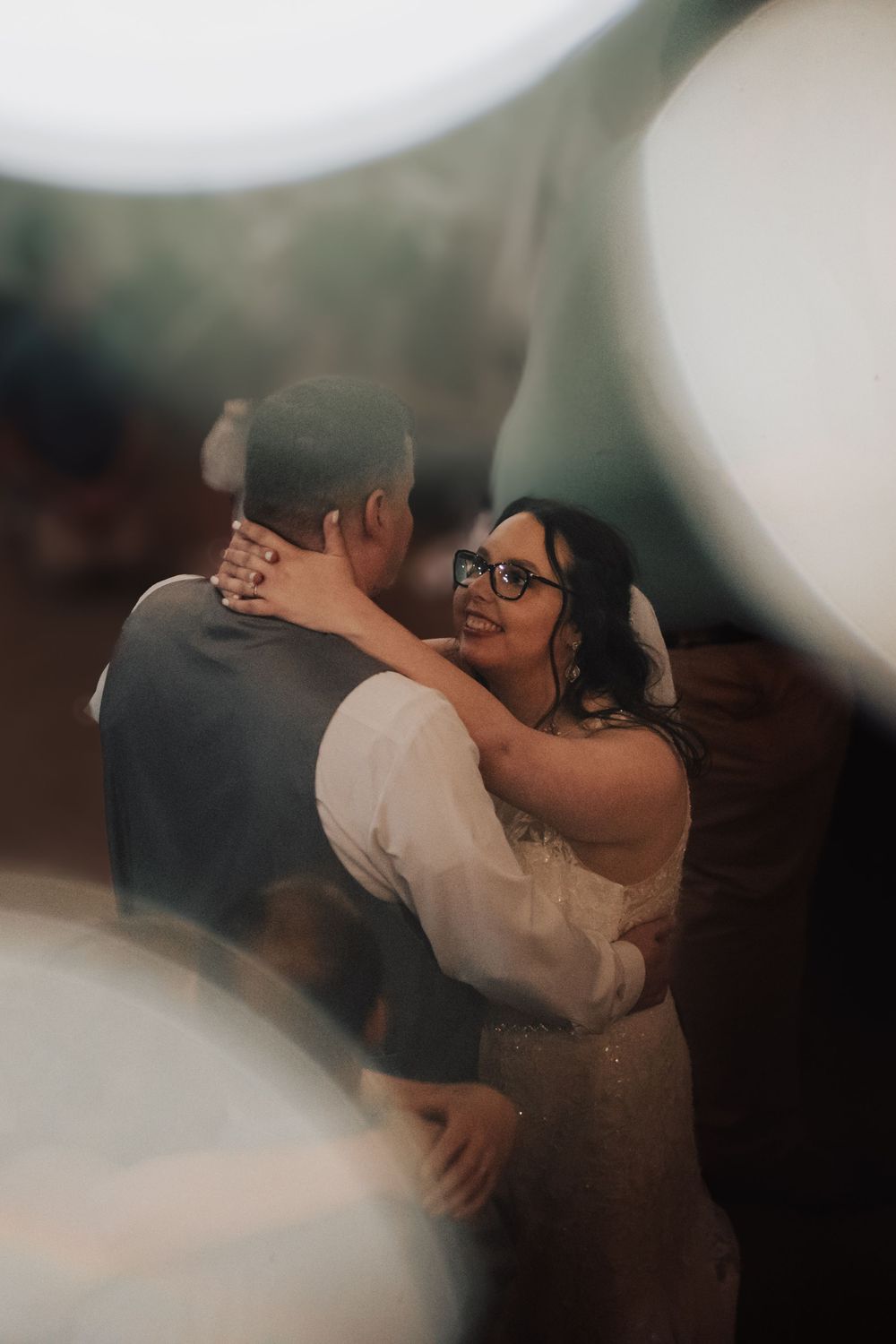 A couple shares a romantic dance moment at a wedding reception captured through a dreamy, soft-focus lens.
