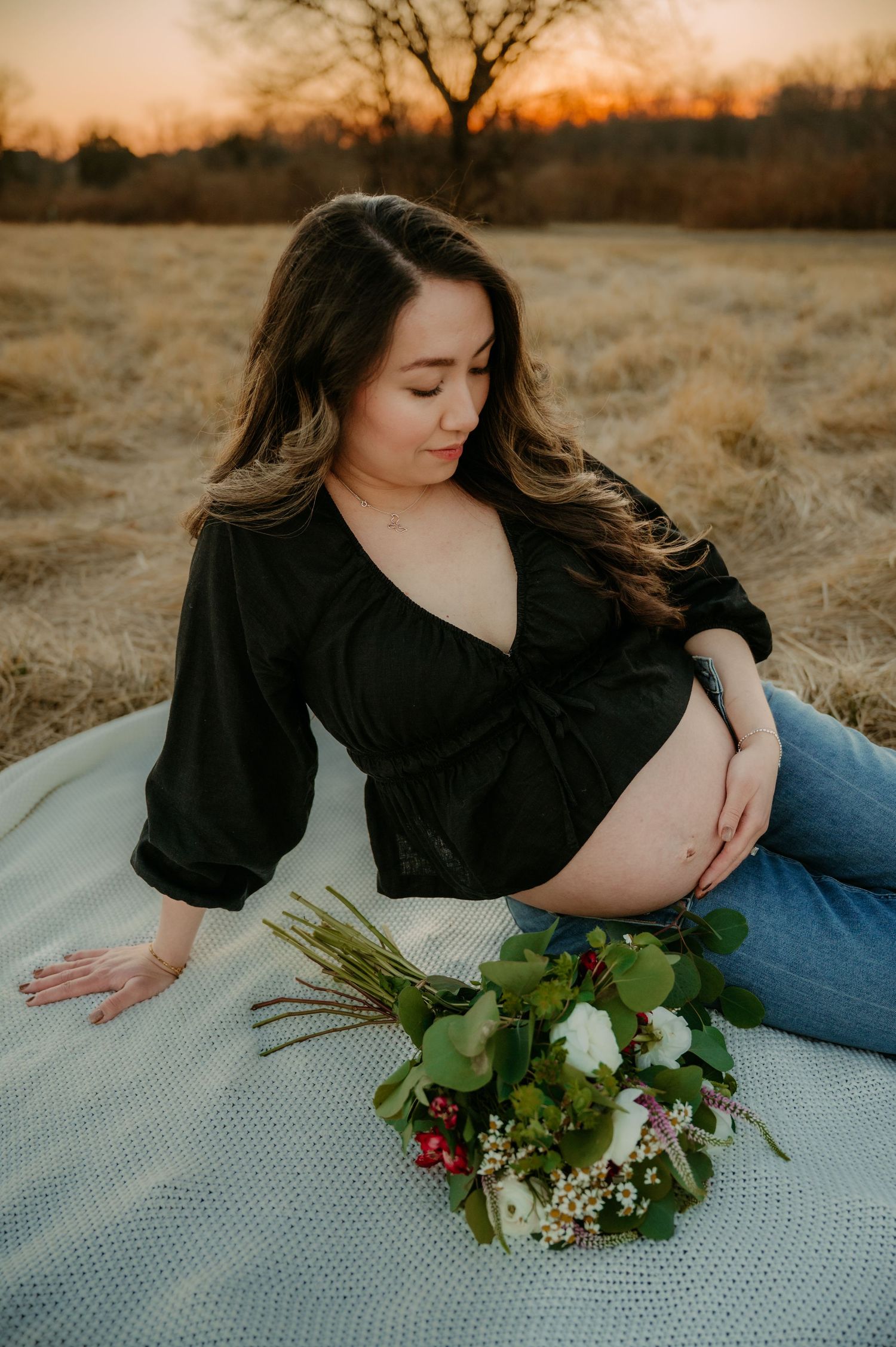 Expecting mother poses on blanket with flowers during outdoor sunset photoshoot in Stafford VA.