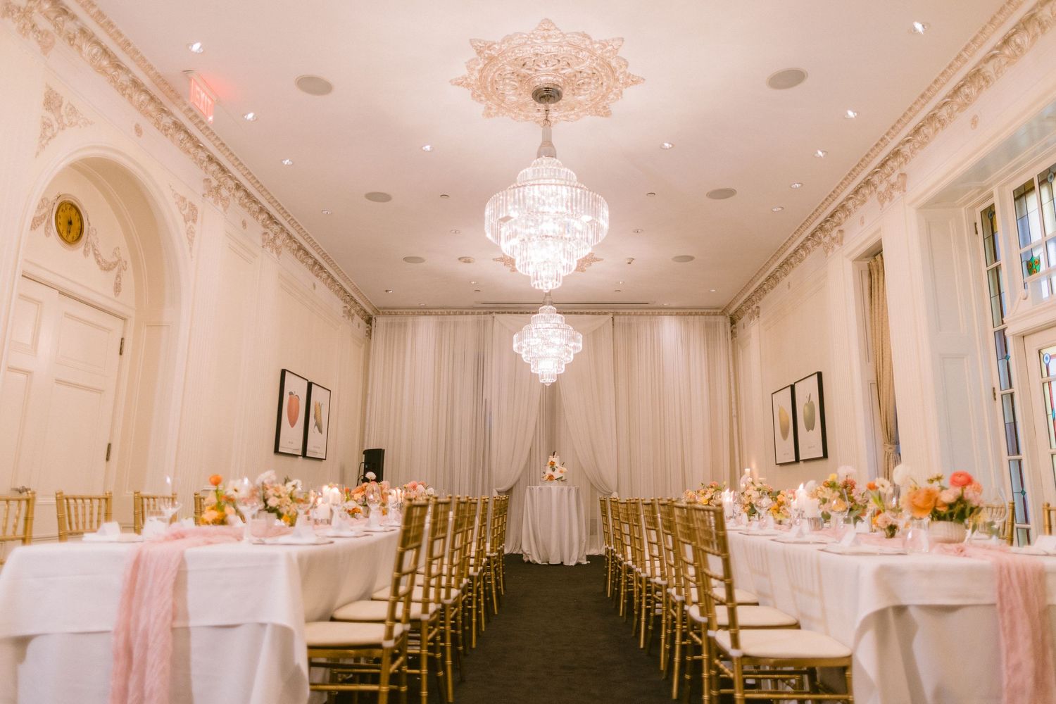 Elegant white wedding reception hall with crystal chandeliers, draped fabric walls, and tables set for a formal event.