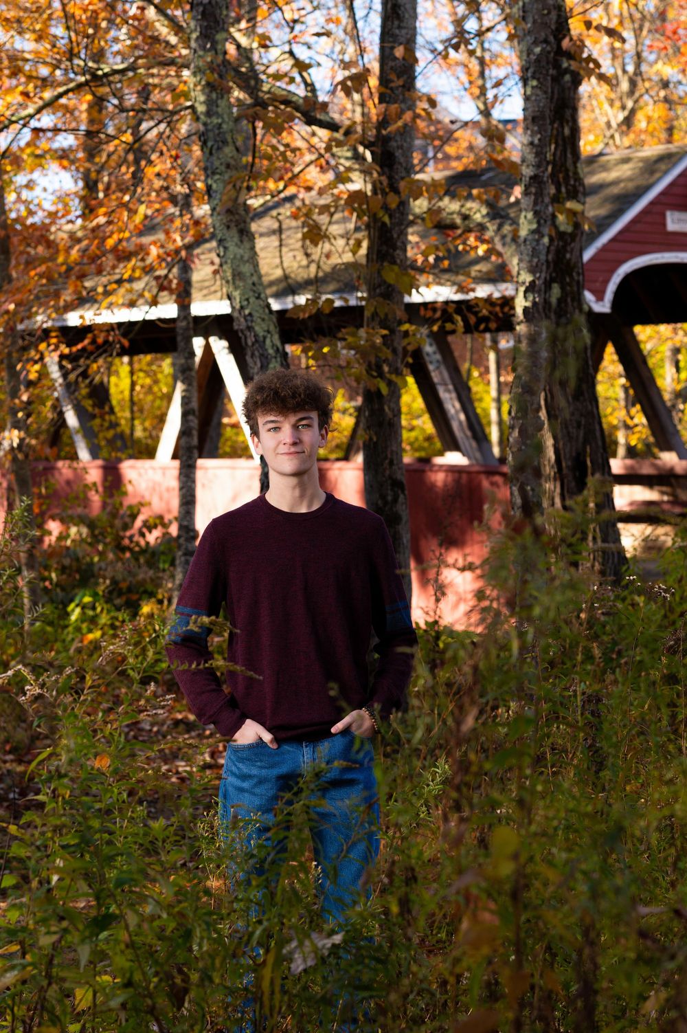 Autumn outdoor portrait session among trees with fall foliage and red barn in background.
