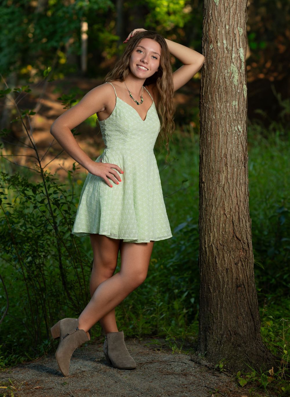 Summer portrait session in mint dress among pine trees.