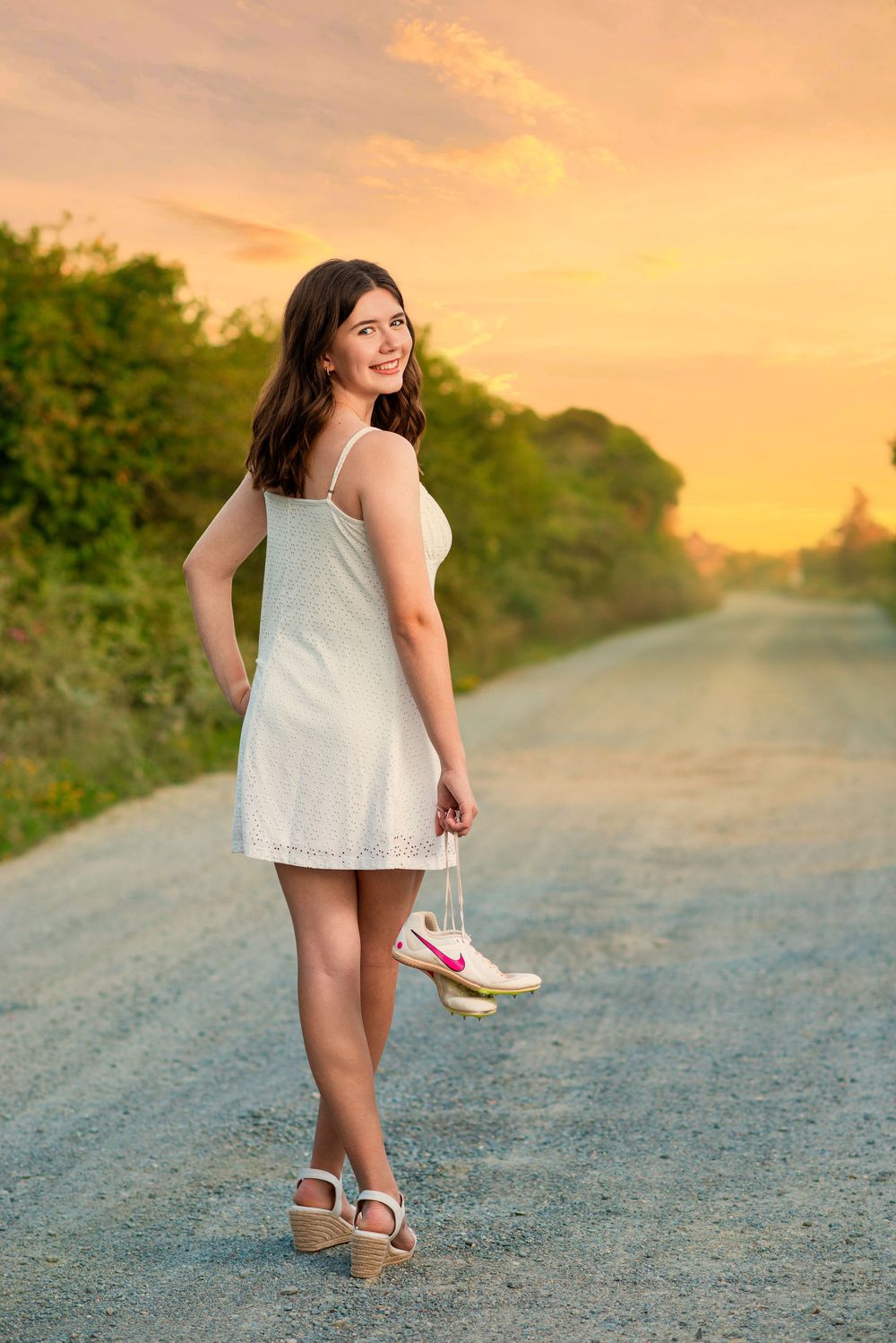 A child in a white dress plays on a gravel path during golden hour sunset.