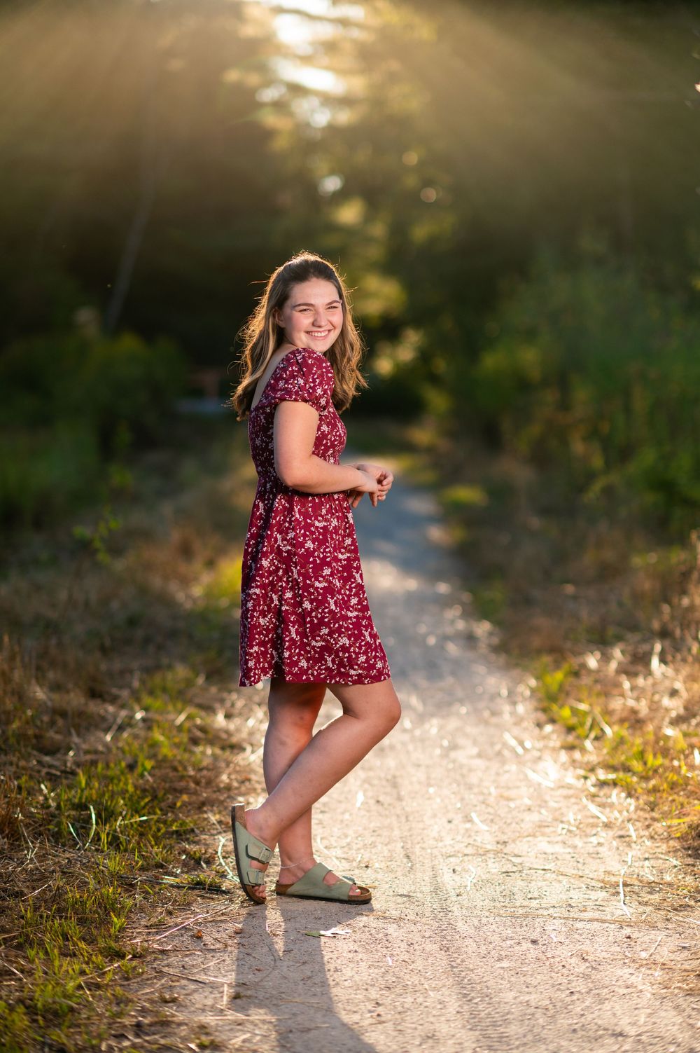 Child in red floral dress dances on sunlit dirt path during golden hour.