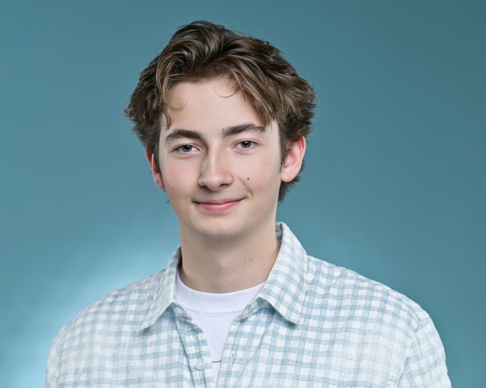 Studio portrait against blue background wearing checkered button-down shirt.