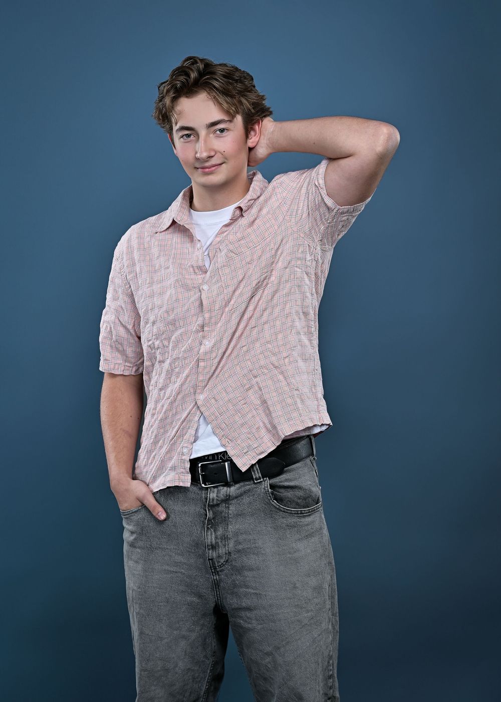 Portrait against blue backdrop wearing pink textured shirt and gray jeans.