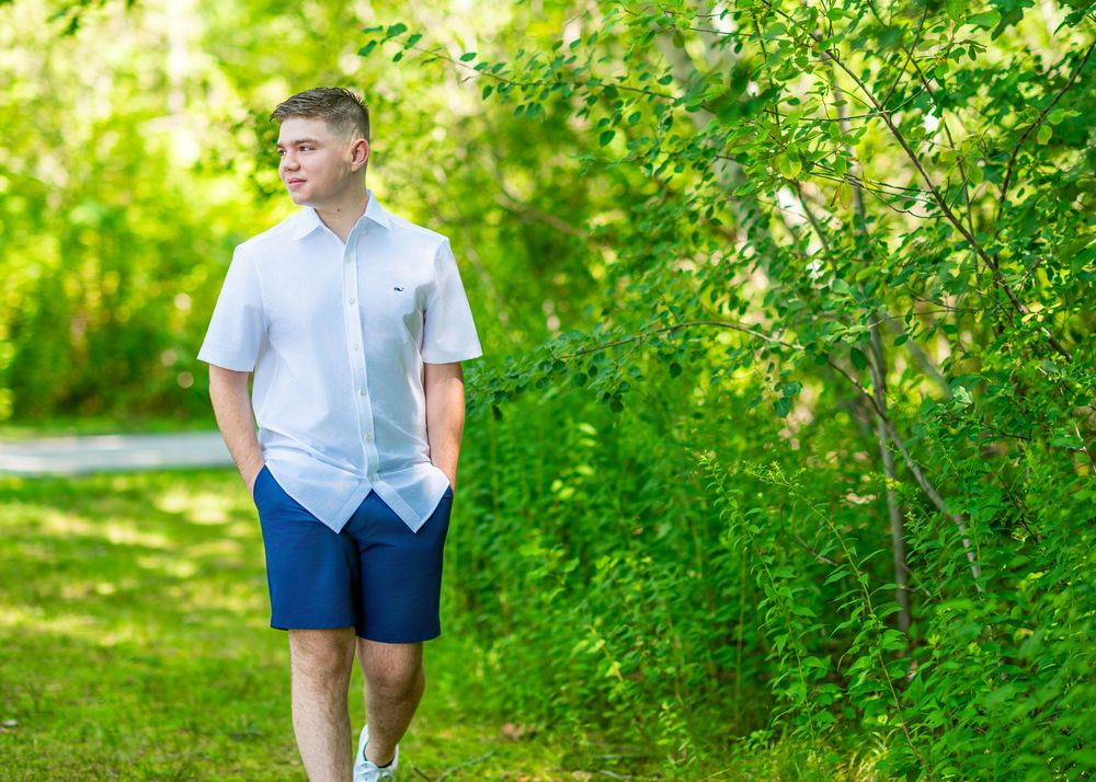 Young person in light colored clothing walks through lush green garden setting.