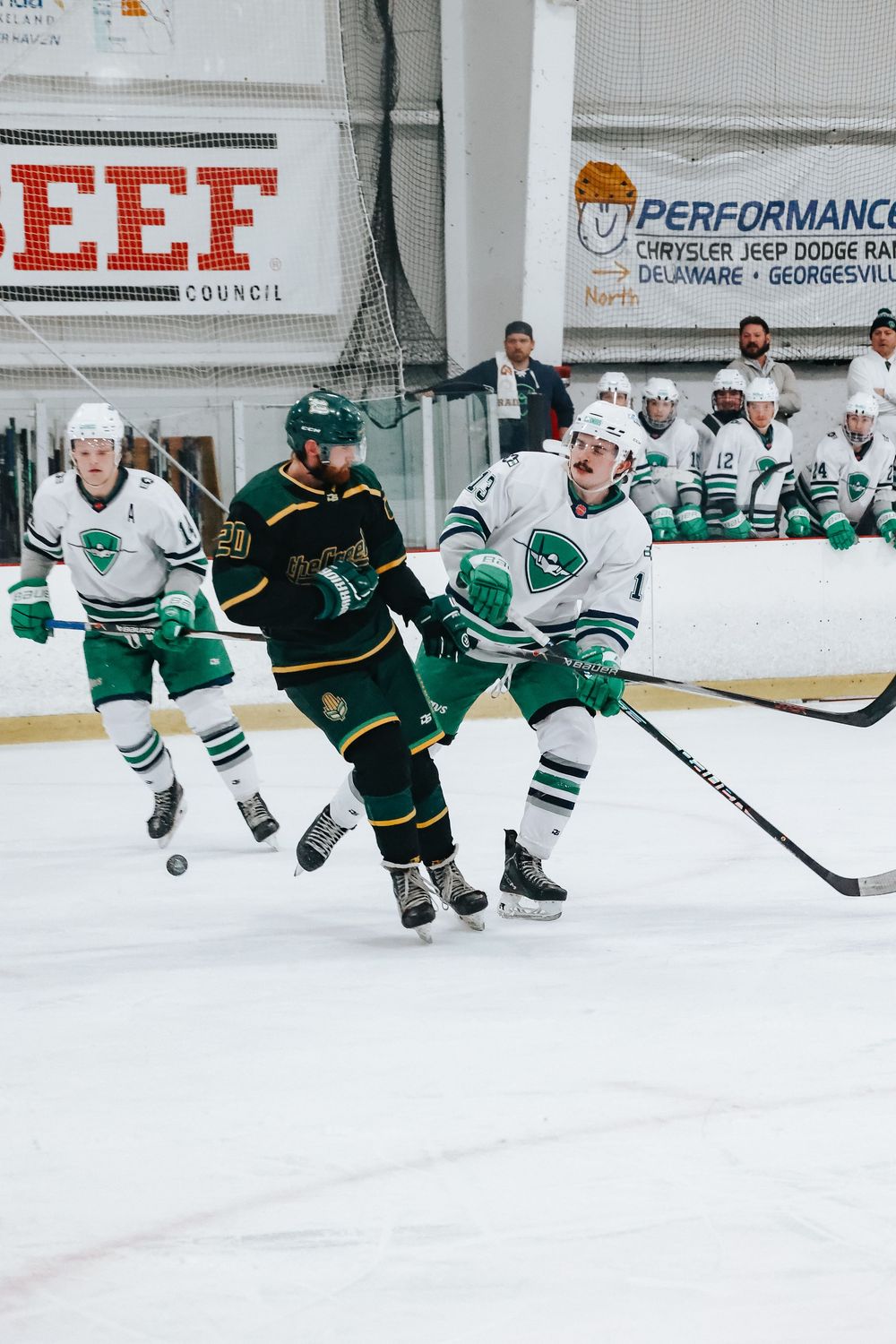 Ice hockey players in green and white jerseys battle for the puck during an intense game.