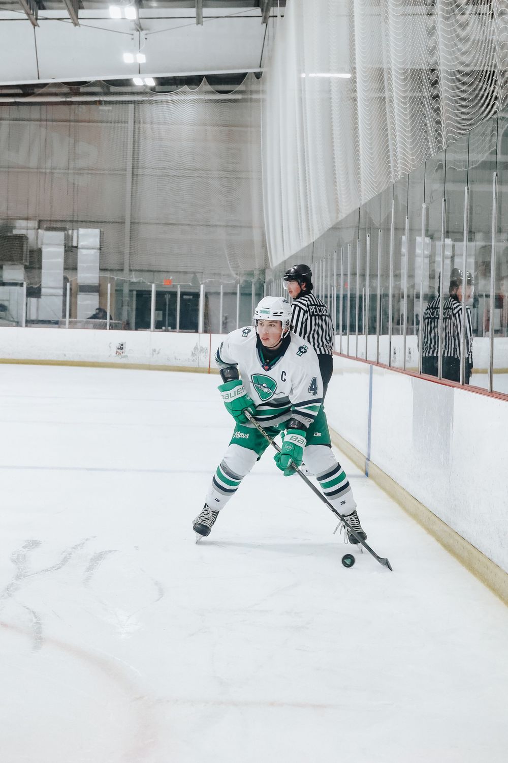 Hockey player in green jersey skates with puck on ice rink during competitive match.