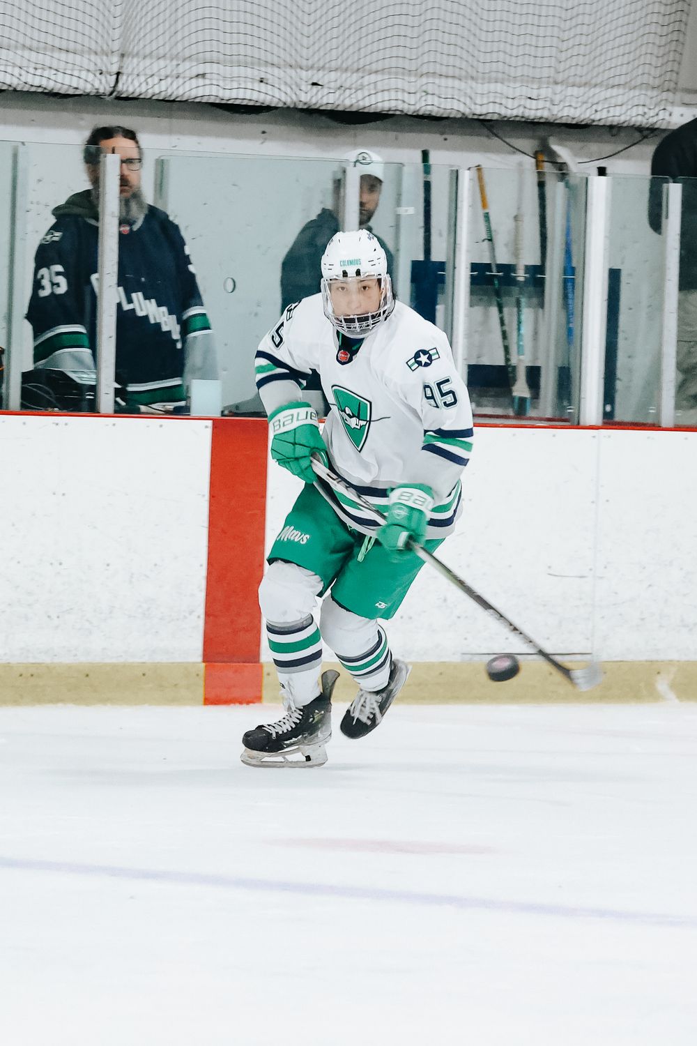 Hockey player in white and green jersey number 15 skates on ice during competitive match.