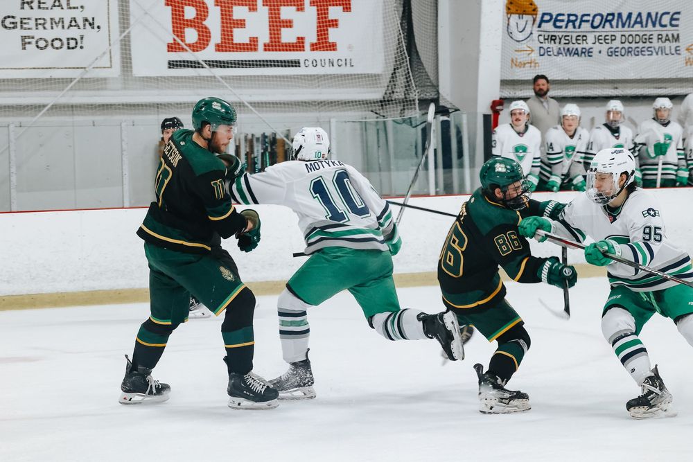 Hockey players from opposing teams battle for the puck during an intense game with green and white uniforms.