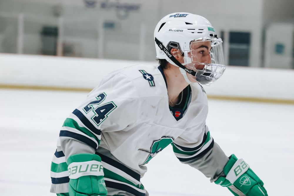 Hockey player in white and green striped jersey skating on ice during competitive match.