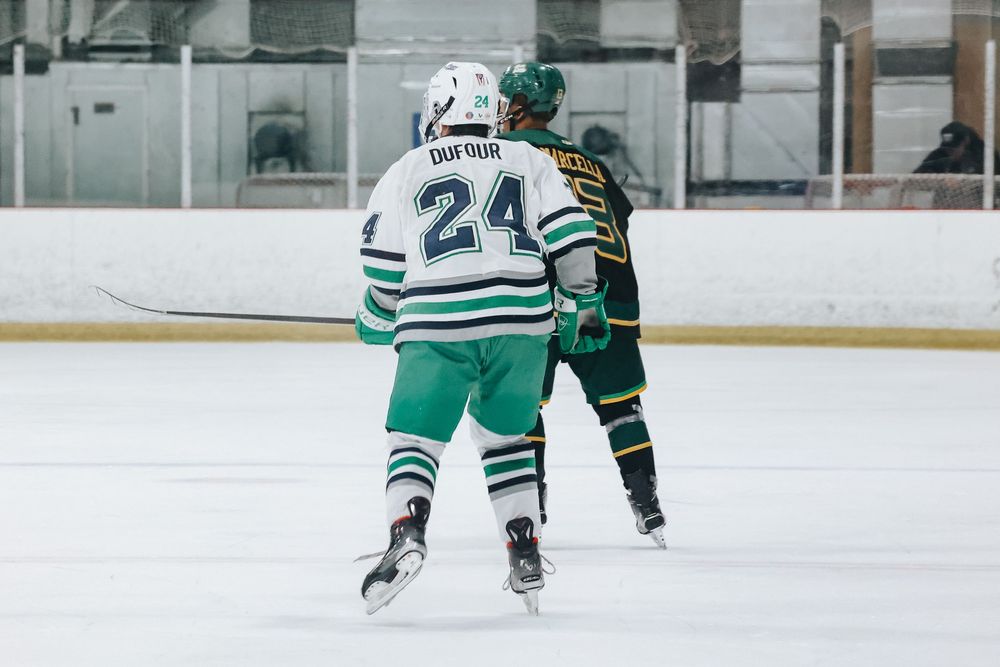 Hockey players in green and white striped jerseys skate on an ice rink during a game.