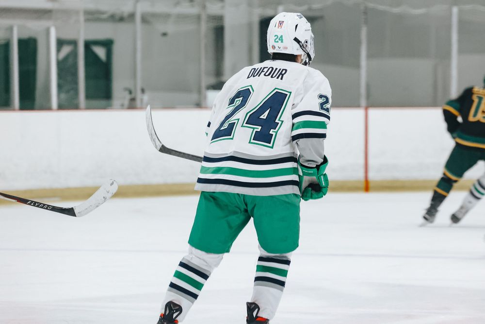 Ice hockey players in white and green uniforms skate on the rink during a competitive game.