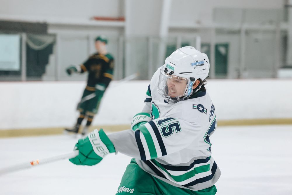 Hockey players in white and green uniforms compete during an intense ice hockey match.