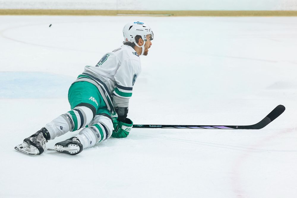 A hockey player in a white and green uniform glides across the ice while making a turn during a game.