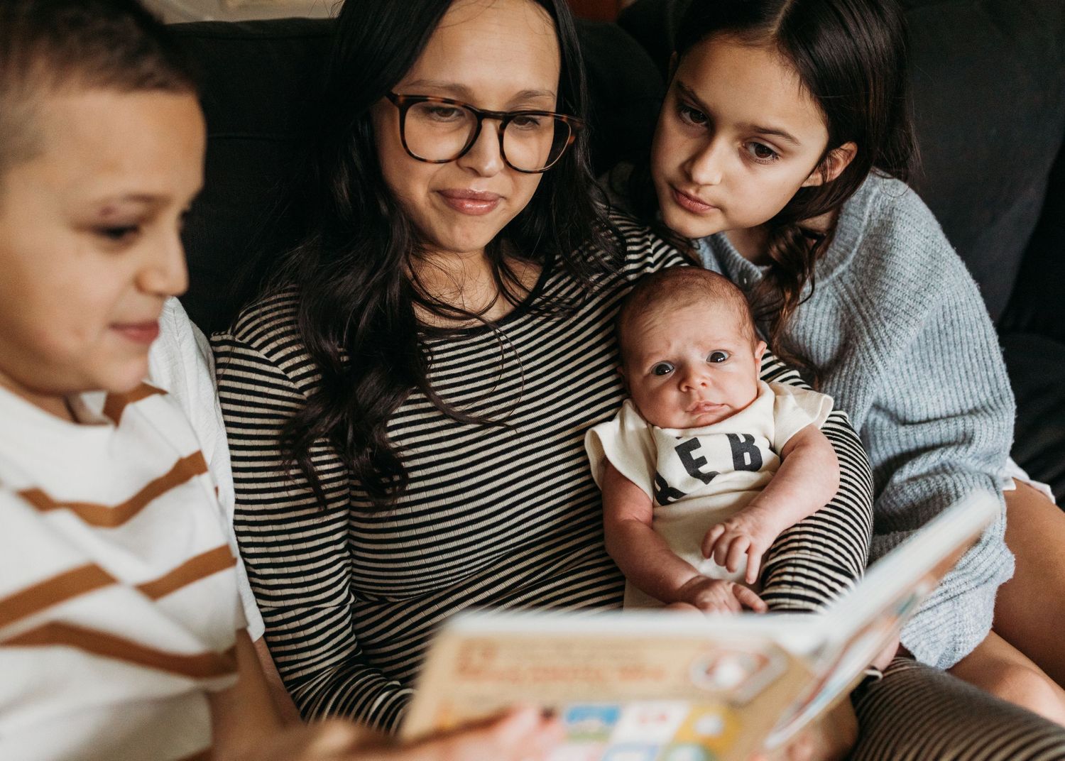 Family sitting together looking at a book in a cozy indoor setting with natural lighting.