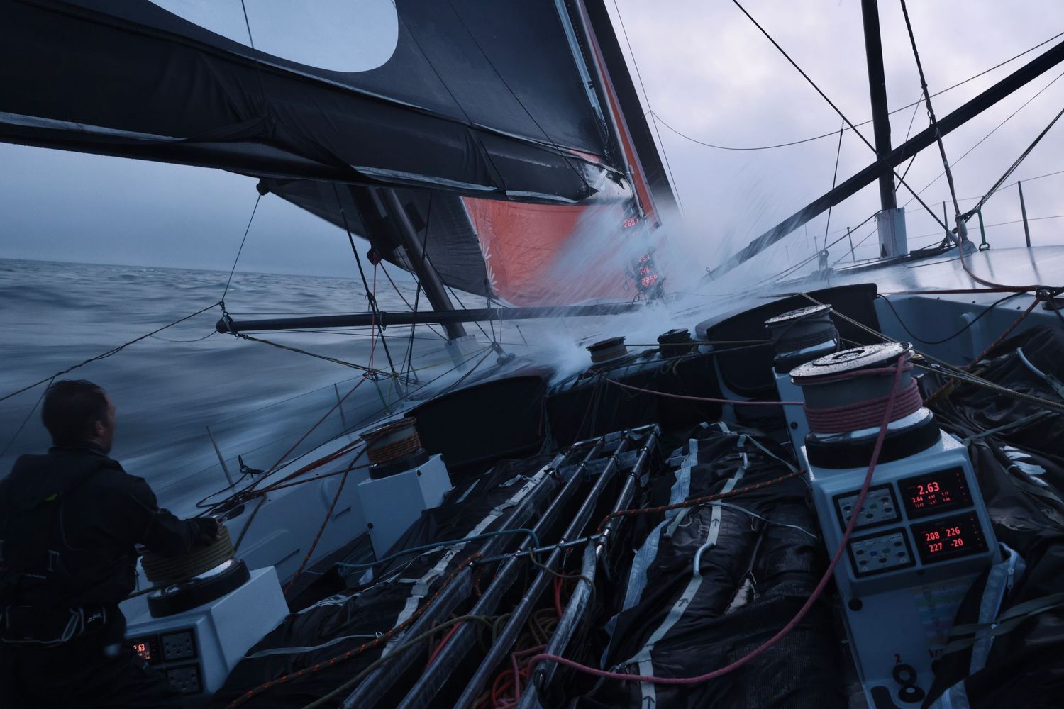 A sailing vessel's white sails and rigging are silhouetted against a dramatic cloudy sky during a voyage at sea.