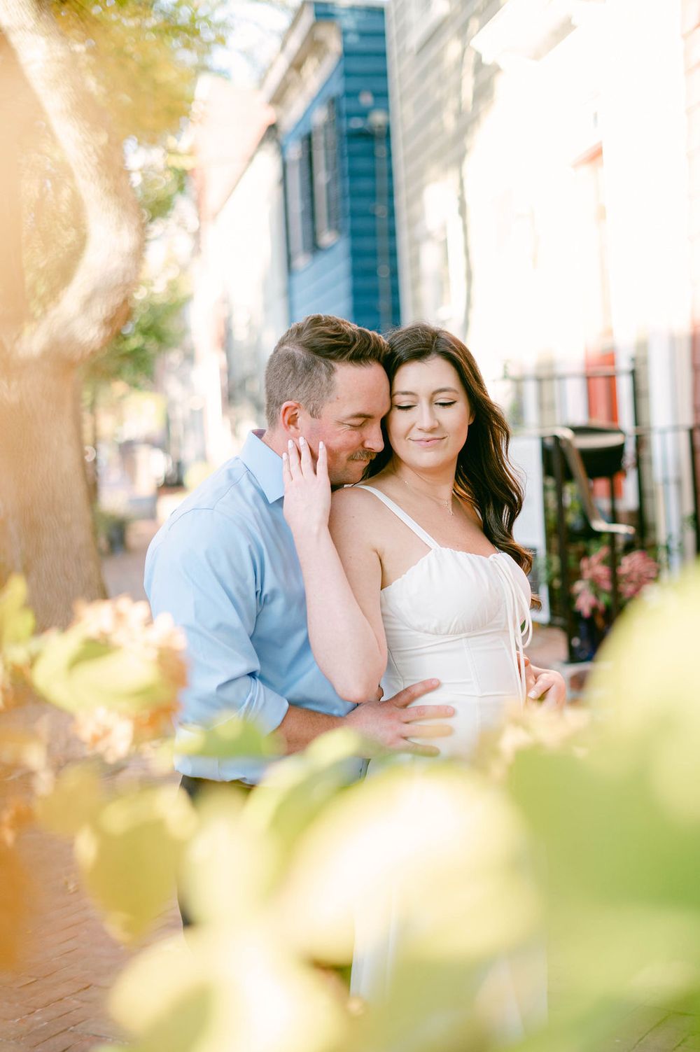 A romantic engagement photo session on a sunlit city street with soft bokeh effects in the foreground.